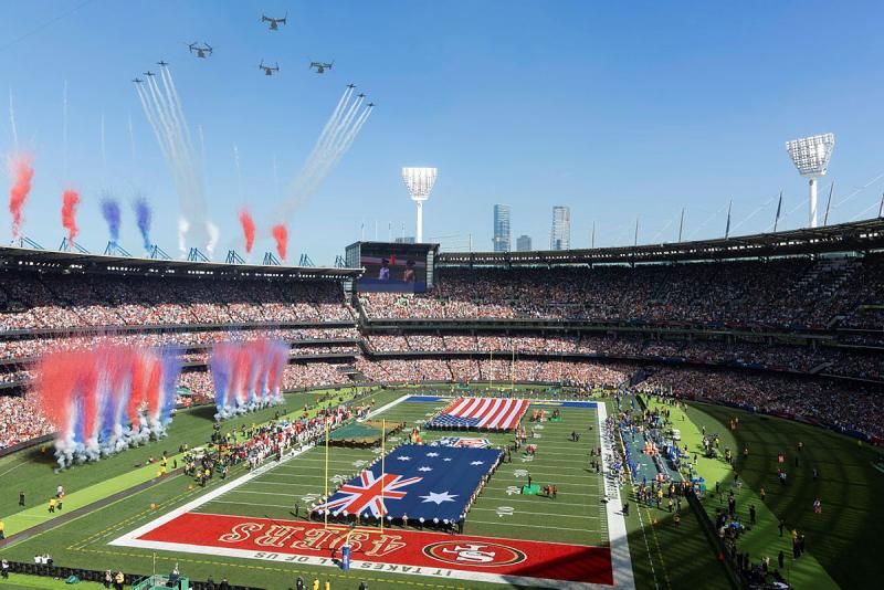 A filled out stadium with US and Australian flags, confetti explosions and aircraft flying in formation.