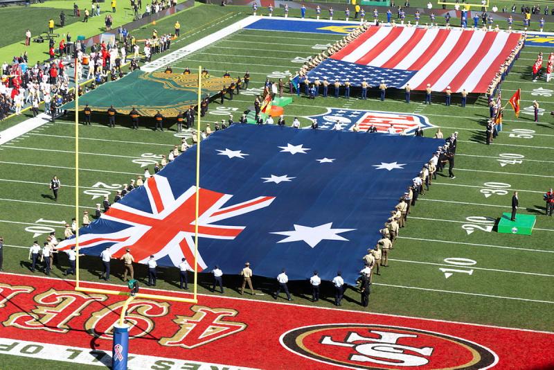 An Australian flag and a United States flag is held up by military personnel on a sports field.