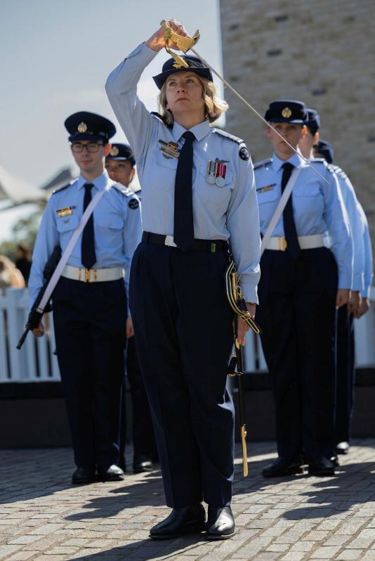 A female aviator holds her sword over her head. Other aviators are seen behind her in the same Air Force uniforms.