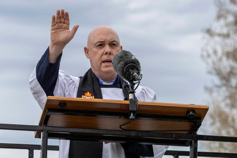 A priest raises his hand as he speaks into the mic at a podium.
