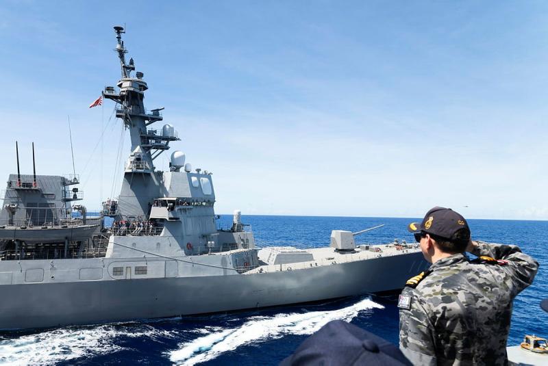 A military man salutes a passing ship at sea.