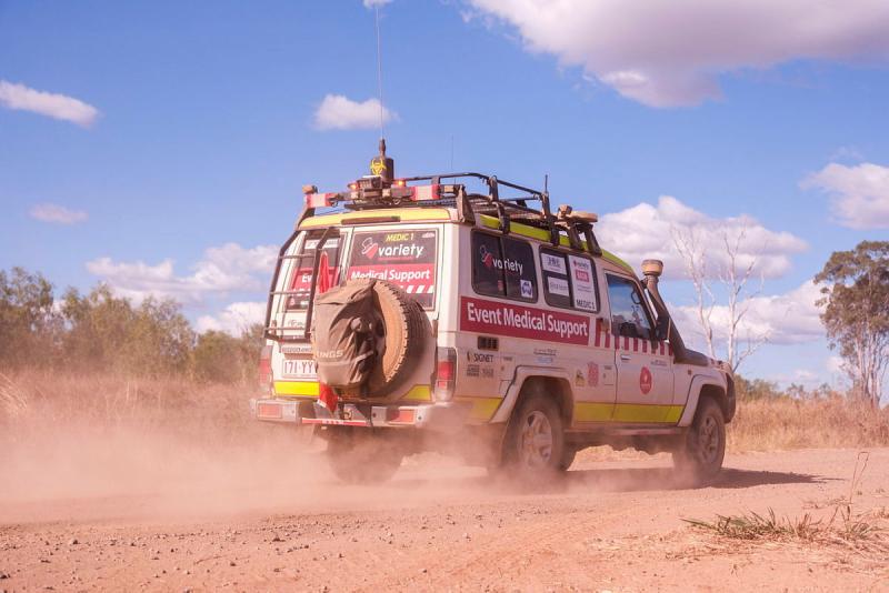A four-wheel-drive vehicle marked "Event Medical Support" travels along a dirt road in a cloud of dust.