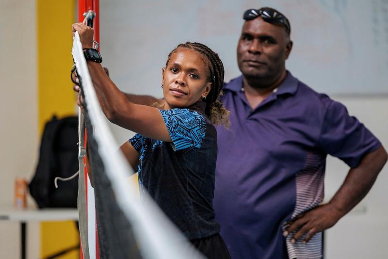 Two Solomon Islander people hold the end of a volleyball net up to a pole.