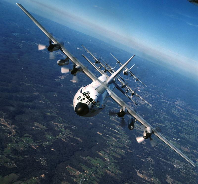 An aircraft flies over fields and straight towards the camera.