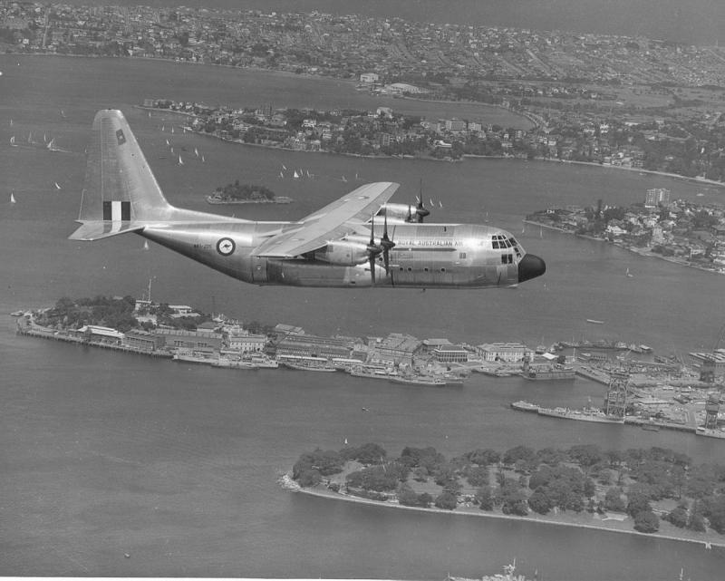 A black and white photo of an aircraft flying over a populated area.