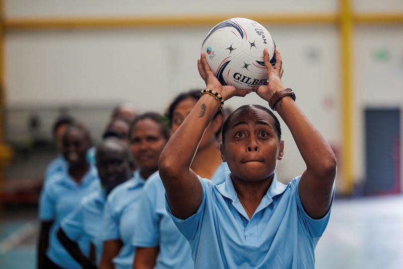 A woman from the Solomon Islands holds a netball above her head. Other women stand behind her in a line.