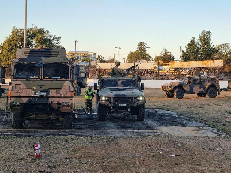 Military personnel refuel several camo vehicles.