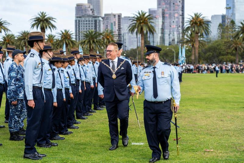 A man with a medallion walks with a military member, surveying a line-up of younger military members.