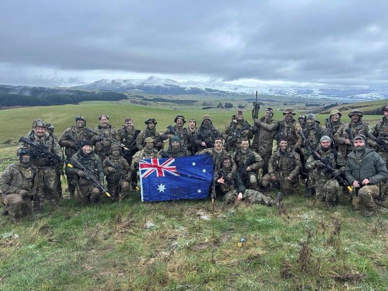 A large group of military personnel with an Australian flag in the middle of a large grassland.
