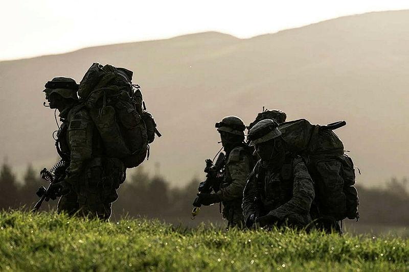 Three soldiers trek through a mountainous region at dusk.