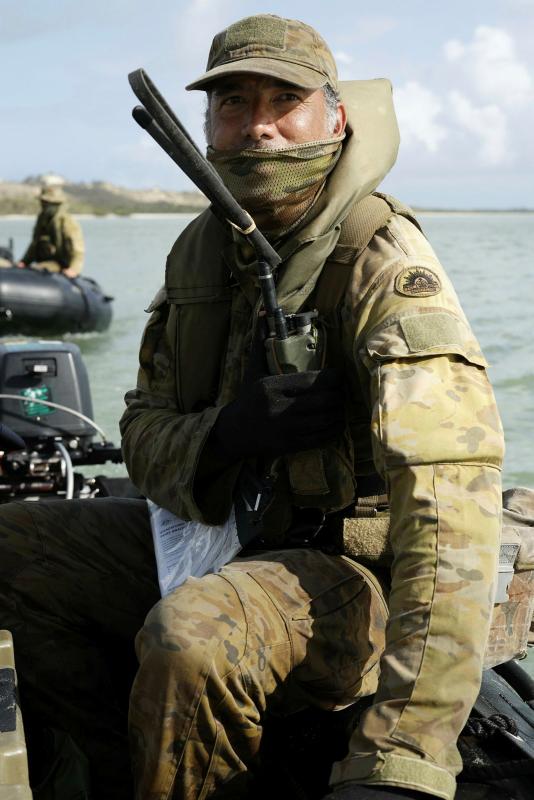 A soldier holds a communication device while on board a small boat in the water.