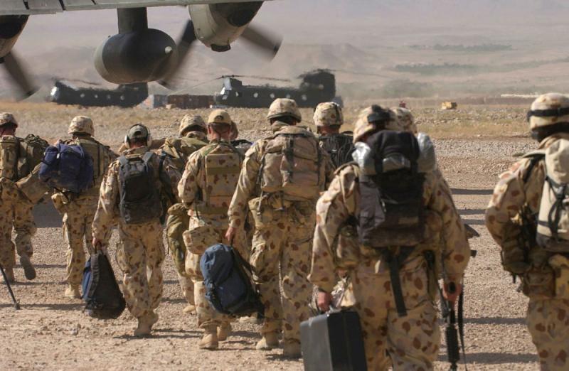 A group of military personnel walk along a dirt airstrip towards an aircraft.