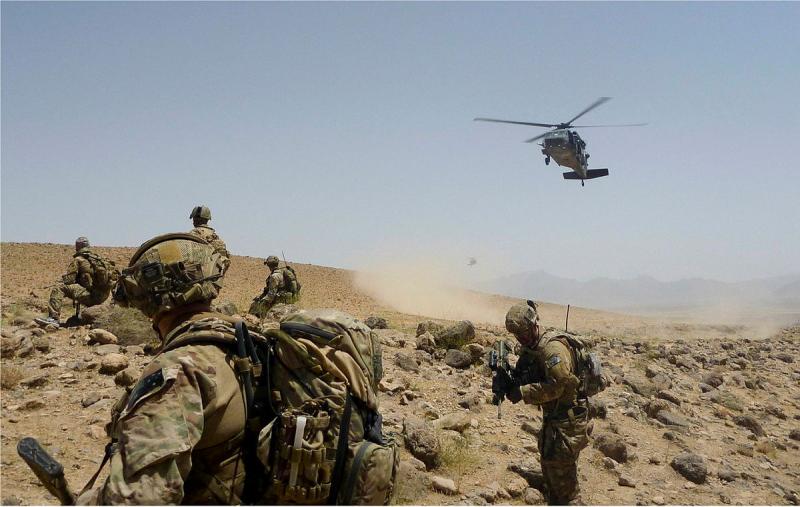 Soldiers in the desert with a helicopter flying overhead.