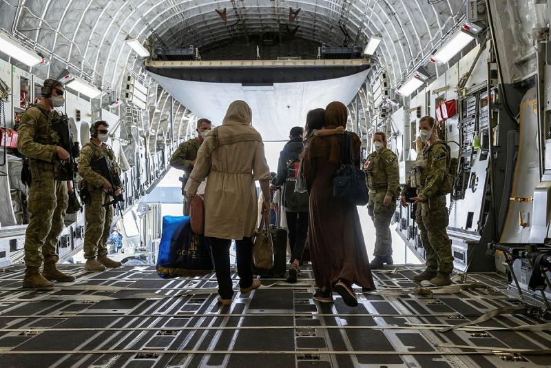 A small group of people walk out the back of an aircraft flanked by five people in military uniform