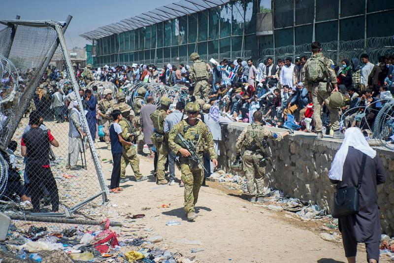 Soldiers patrol as large groups of people gather behind barriers.