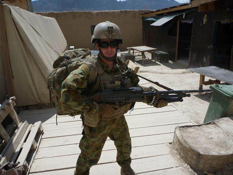 A military man in full gear, with a backpack and large gun strapped over his shoulder.