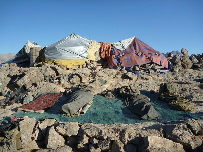 A makeshift tent construction and several soldiers sleeping on a rocky surface.