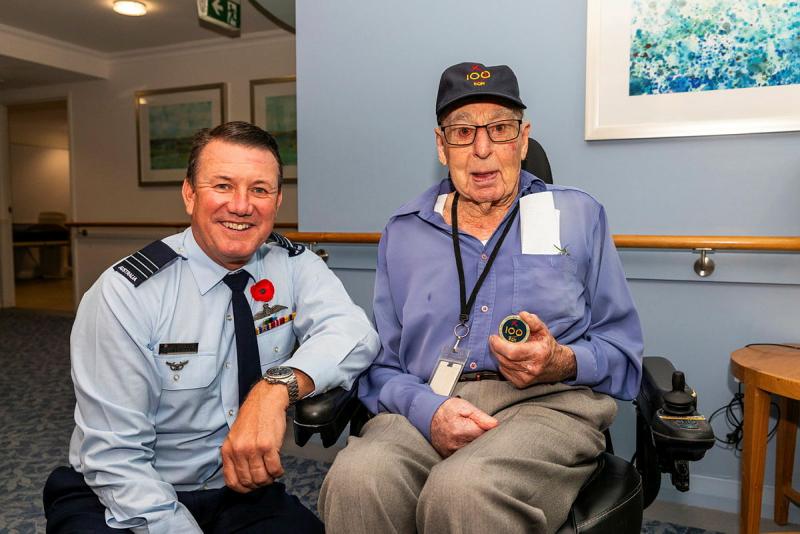 A man in uniform crouches next to an elderly man holding a coin.