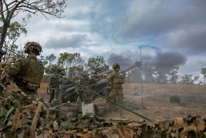 Soldiers stand near a Howitzer with smoke lingering in the air.