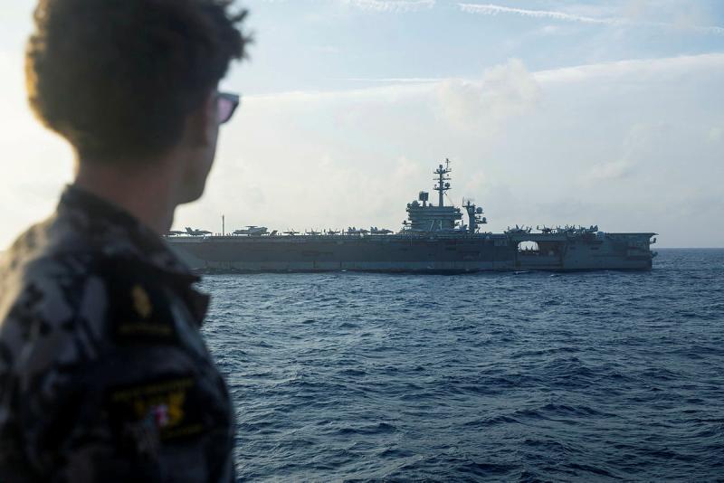A military member looks at at a ship at sea.