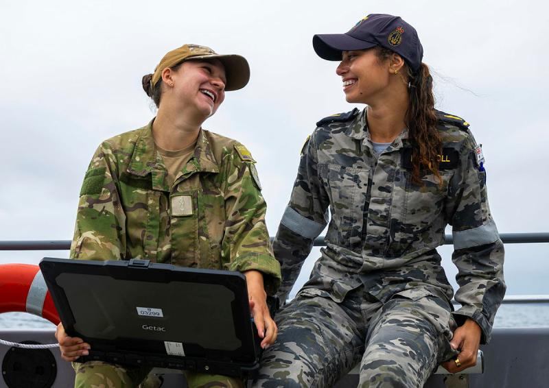 Two military women on a boat laugh together.