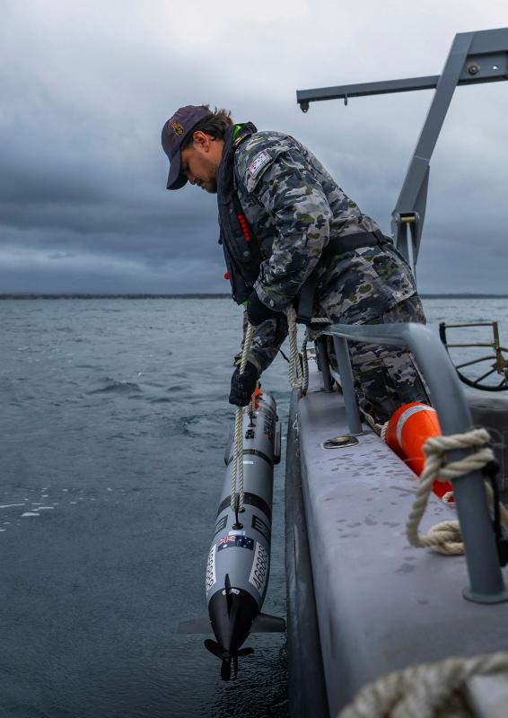 A military man drops a missile-like device off the side of a boat.