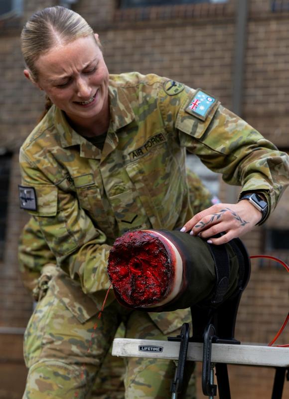 A female soldier wraps a simulated leg injury.