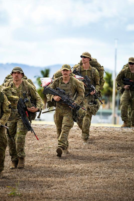 A line of armed soldiers march over a hill.