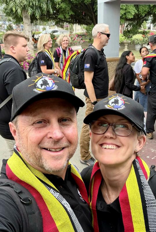 A woman and a man wearing matching hats and scarves take a selfie in public.