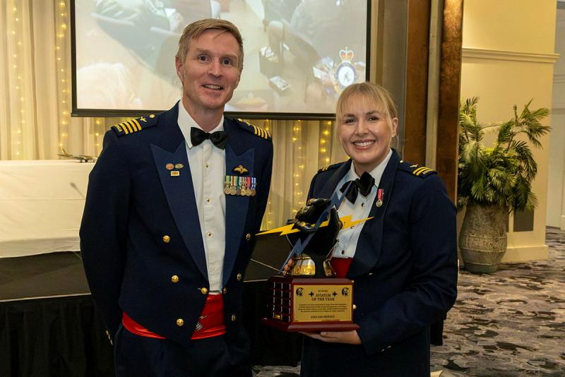 A military woman holds a trophy next to a military man.