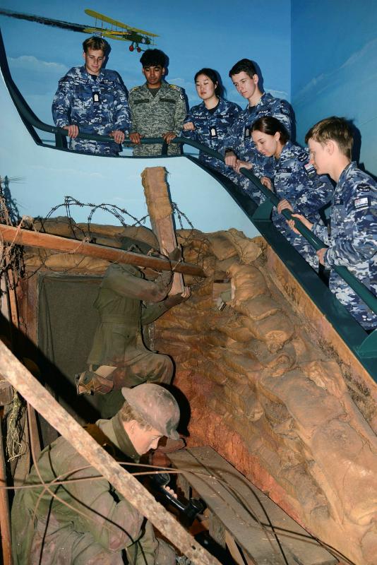 A group of young people in military uniform look at a fake 3D scene of military men at a bunker.