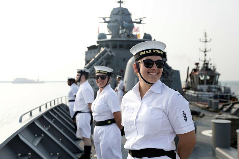 Sailors smile as they stand on a ship.