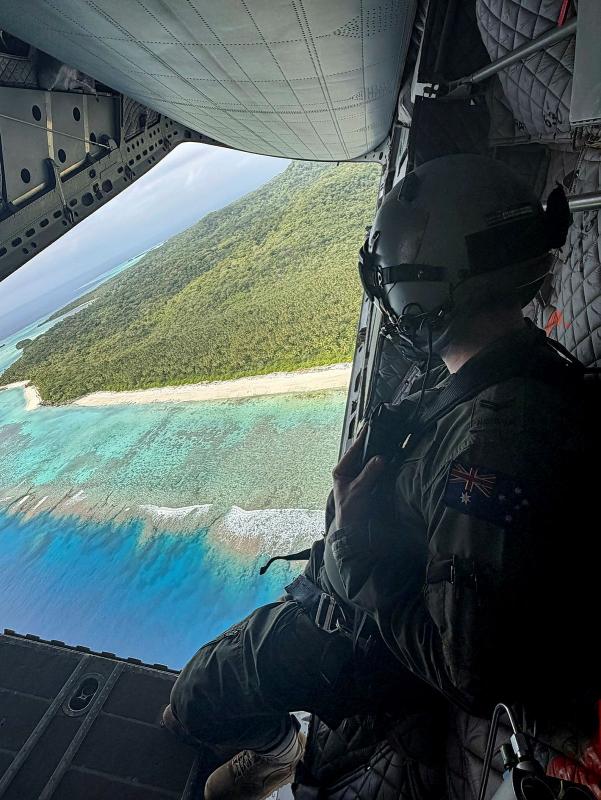 A military person wearing a helmet looks out of aircraft at an island.