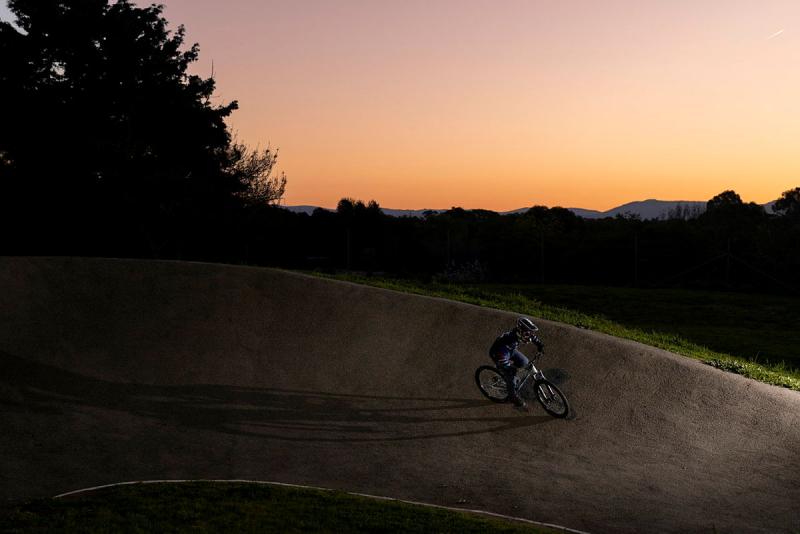 A lone cyclist rides along a steep, angled road on a hill at sunset