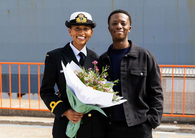 A sailor holds a bunch of flowers.