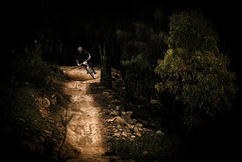 Cyclist in a helmet prepares to cycle down a dirt path through a dark forest