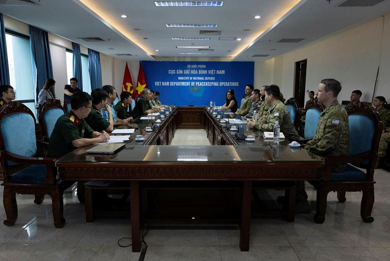 A group of military members sit at a long table for a meeting.