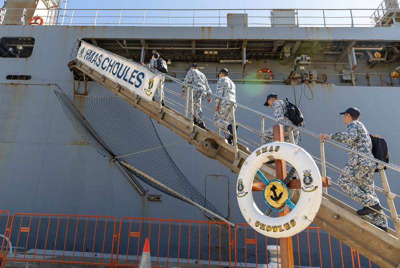 People in uniform proceed up a walkway that goes from the ground onto a ship.