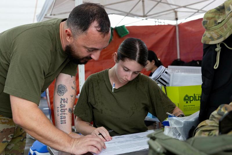 Two military people look over a document in a temporary tent structure.
