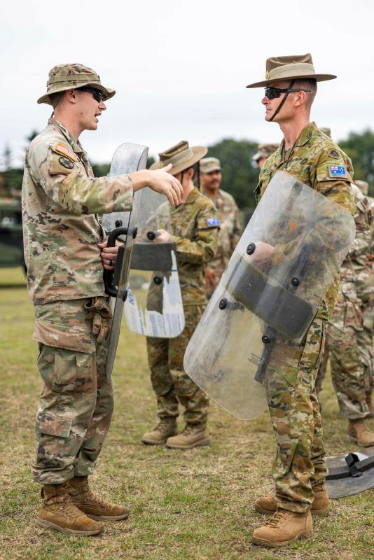 Two men in uniform talk while holding riot shields.