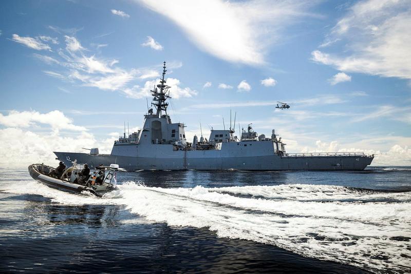A small boat speeds towards a ship with a helicopter nearby.
