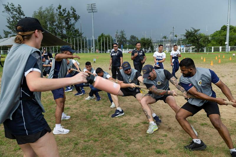 A team of men and women tug on a rope outside.