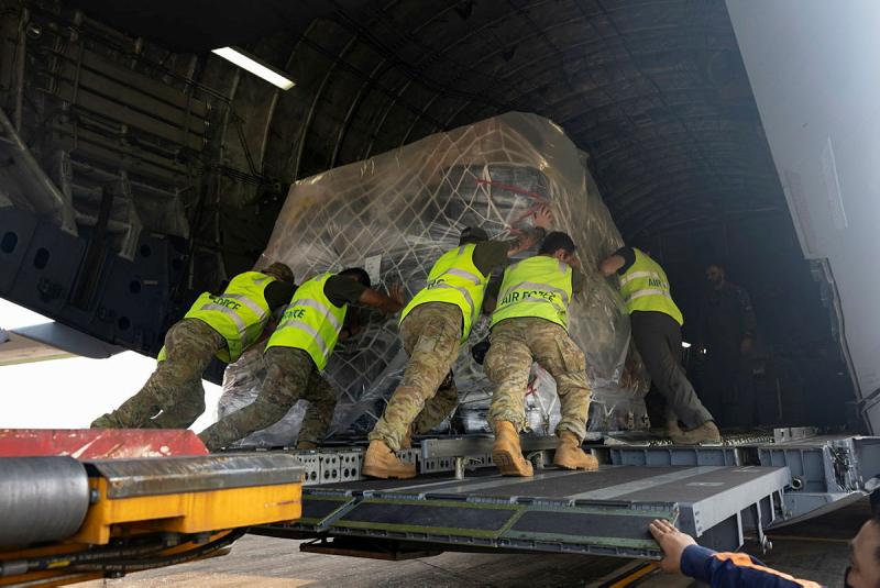 Five men push a huge package of supplies onto a plane.