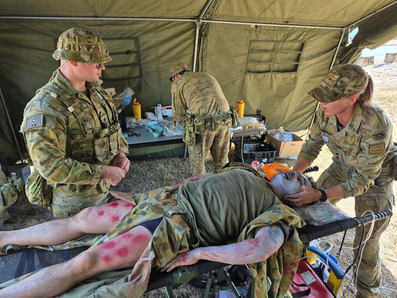 Army members treat a pretend burns casualty in a tent medic station.