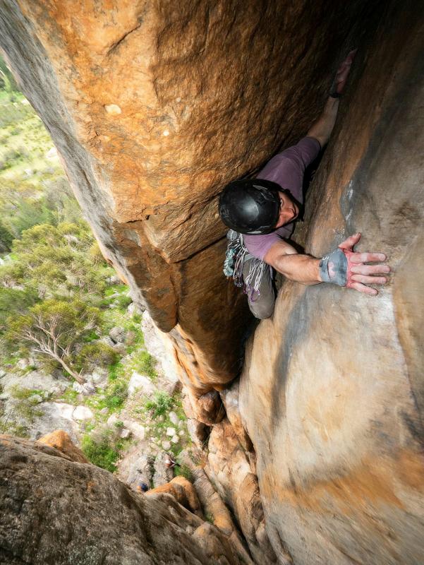 A man in rock climbing gear clings to a rocky cliff face.