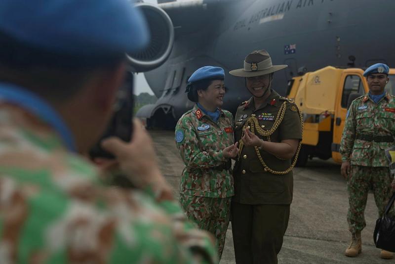 A military person takes a photo of two military woman smiling and standing close.