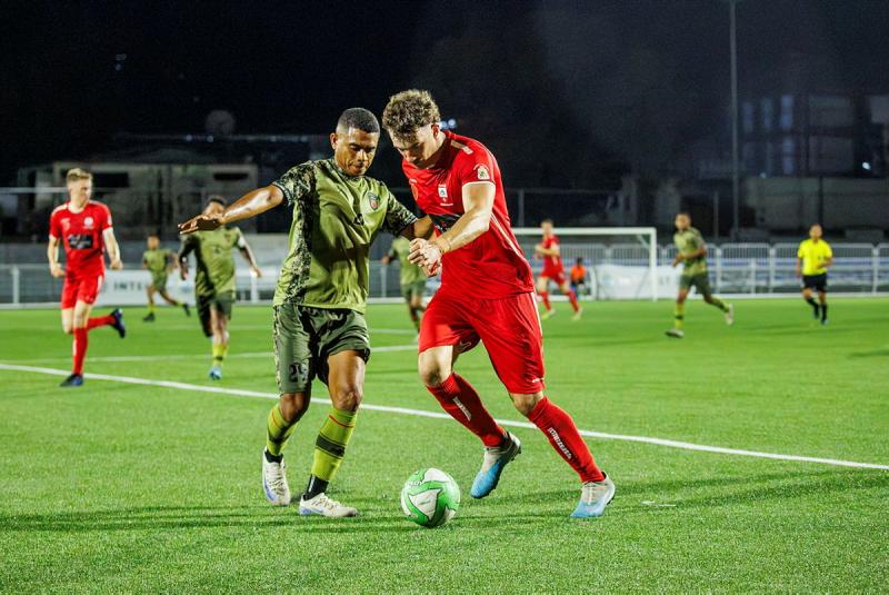 Two opposing male soccer players fight for the ball during a game.