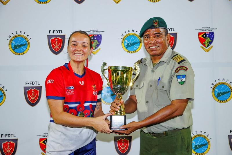 A military man and a female athlete hold a trophy.