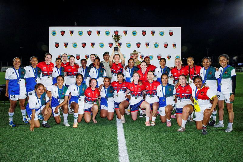 Two teams of female soccer players group together with their medals and trophy.
