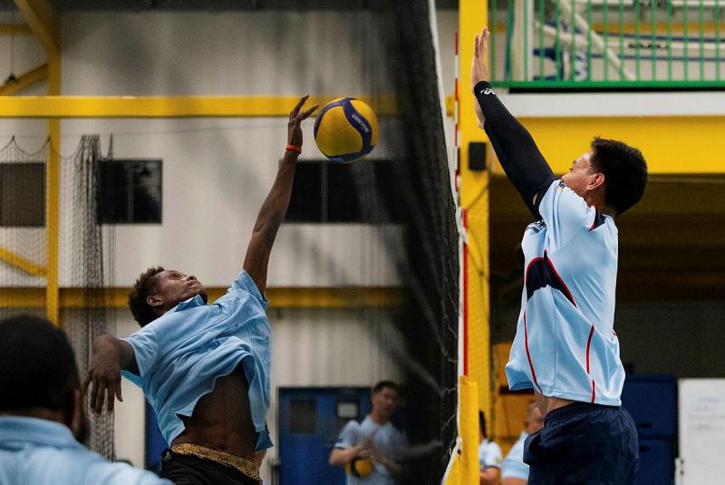 Two men leap up for the ball in a volleyball game.